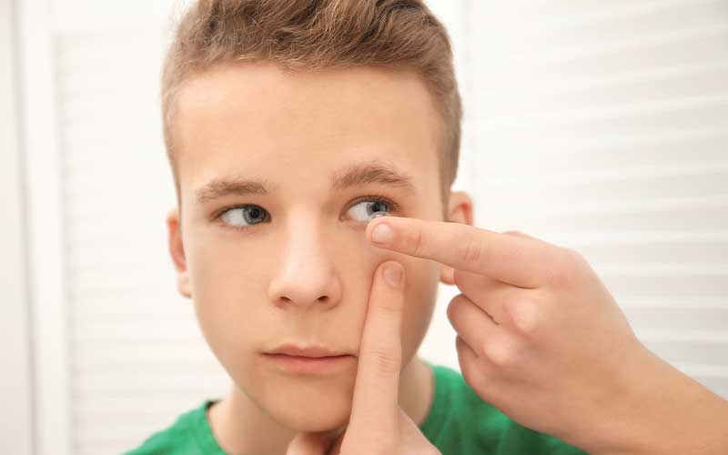 Boy putting on contacts in front of a mirror.